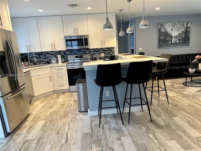 kitchen featuring sink, appliances with stainless steel finishes, hanging light fixtures, white cabinets, and a kitchen island