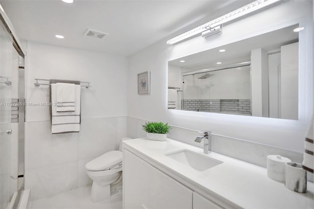 bathroom featuring vanity, toilet, a shower with shower door, and tile walls