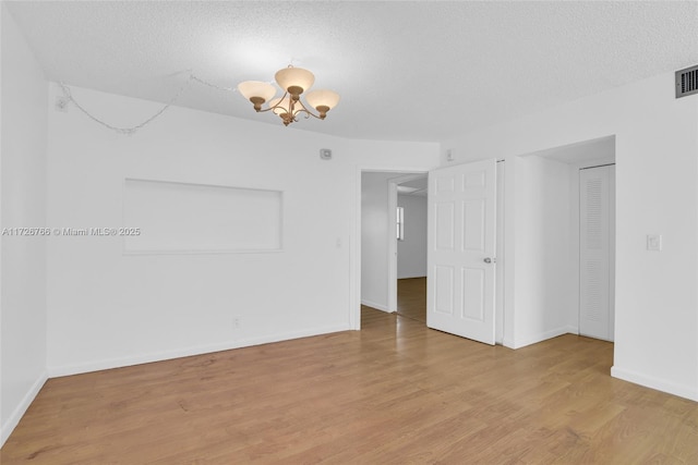 empty room featuring a textured ceiling, an inviting chandelier, and light hardwood / wood-style floors