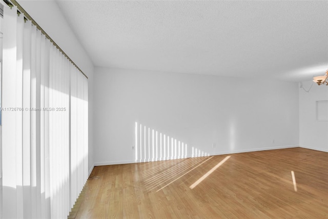 unfurnished room with light wood-type flooring, a notable chandelier, and a textured ceiling