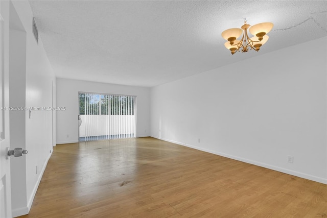 empty room with light wood-type flooring, a chandelier, and a textured ceiling