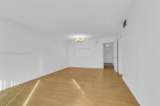 unfurnished room with a textured ceiling, a chandelier, and light hardwood / wood-style floors