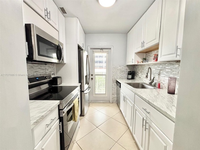 kitchen with sink, light tile patterned floors, appliances with stainless steel finishes, white cabinets, and light stone counters