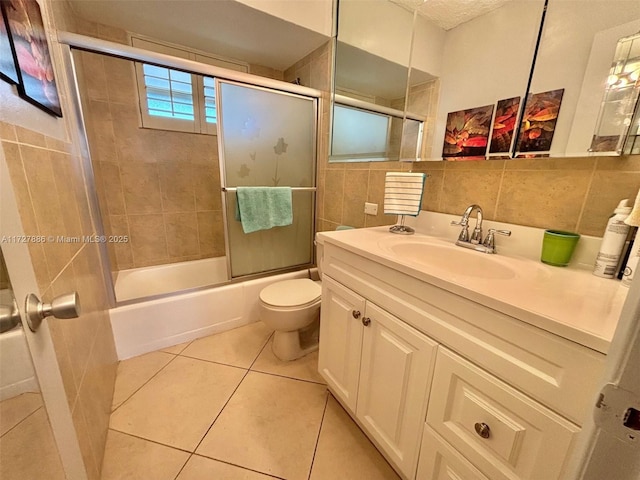 full bathroom featuring tile patterned floors, vanity, tile walls, toilet, and combined bath / shower with glass door