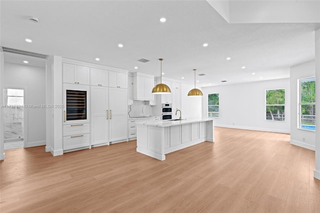 kitchen with light wood-type flooring, white cabinetry, a center island with sink, and decorative light fixtures