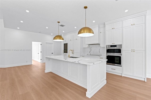 kitchen featuring light stone countertops, a large island with sink, decorative light fixtures, white cabinetry, and sink