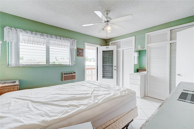 bedroom with ceiling fan, a wall unit AC, light tile patterned flooring, multiple closets, and a textured ceiling