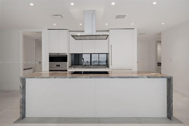 kitchen featuring stainless steel double oven, white cabinets, a kitchen island, island range hood, and light stone counters