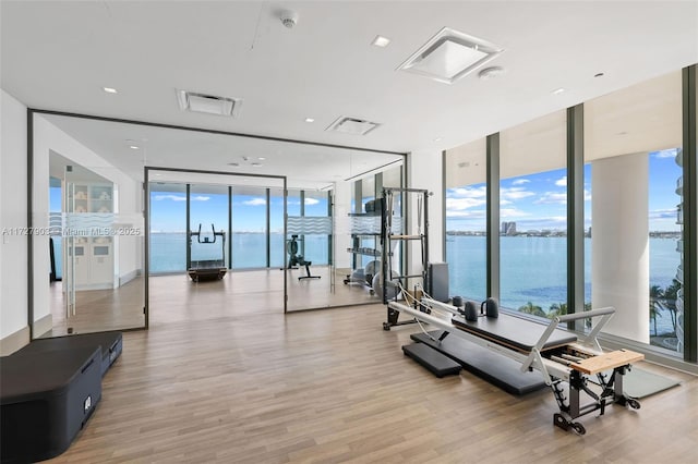 workout area with floor to ceiling windows, a wealth of natural light, a water view, and light hardwood / wood-style flooring