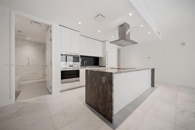 kitchen featuring white cabinetry, stainless steel double oven, island exhaust hood, a center island, and sink