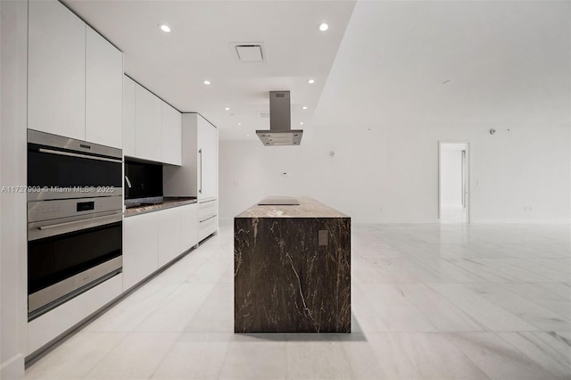 kitchen featuring stainless steel double oven, white cabinetry, island exhaust hood, and a kitchen island