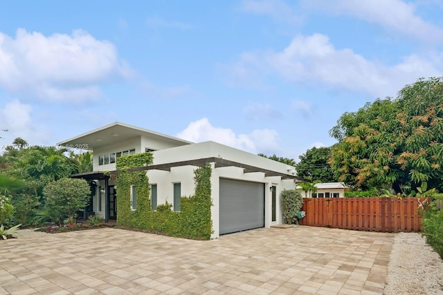 view of home's exterior with decorative driveway, stucco siding, an attached garage, and fence