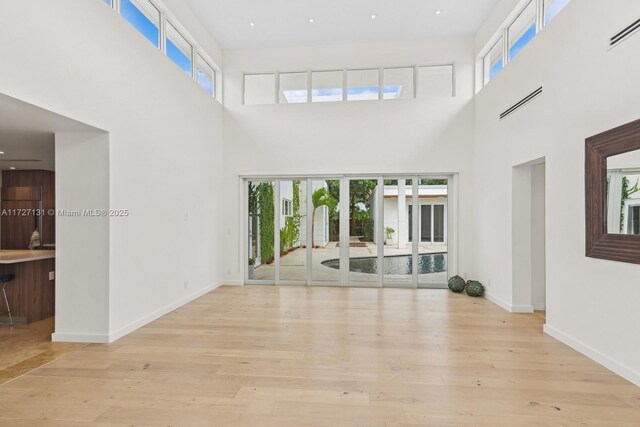 unfurnished living room featuring french doors, light hardwood / wood-style flooring, and a high ceiling