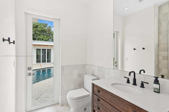 bathroom featuring a wainscoted wall, toilet, tile walls, and vanity