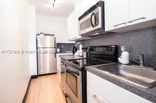 kitchen featuring appliances with stainless steel finishes, white cabinetry, tasteful backsplash, light hardwood / wood-style floors, and sink