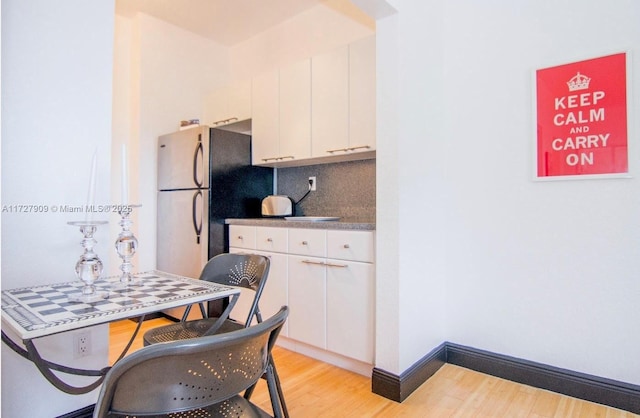 kitchen with light wood-type flooring, decorative backsplash, stainless steel fridge, and white cabinetry