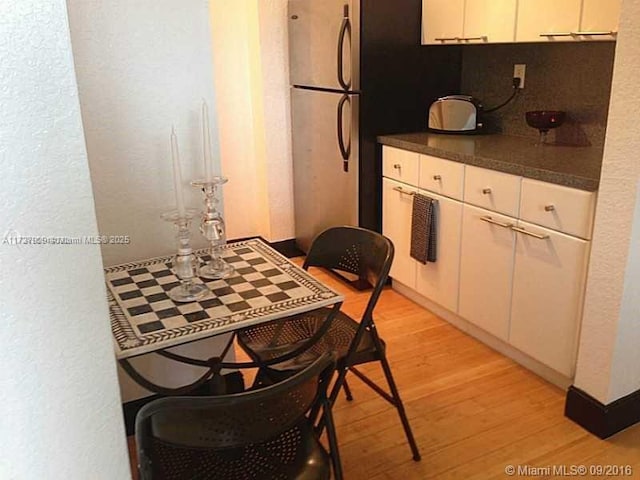 kitchen featuring light hardwood / wood-style floors, white cabinetry, stainless steel fridge, and decorative backsplash