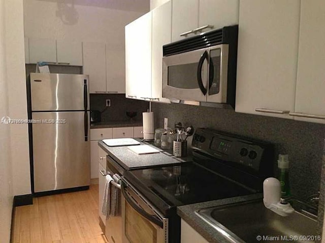 kitchen featuring white cabinets, decorative backsplash, stainless steel appliances, and light hardwood / wood-style floors