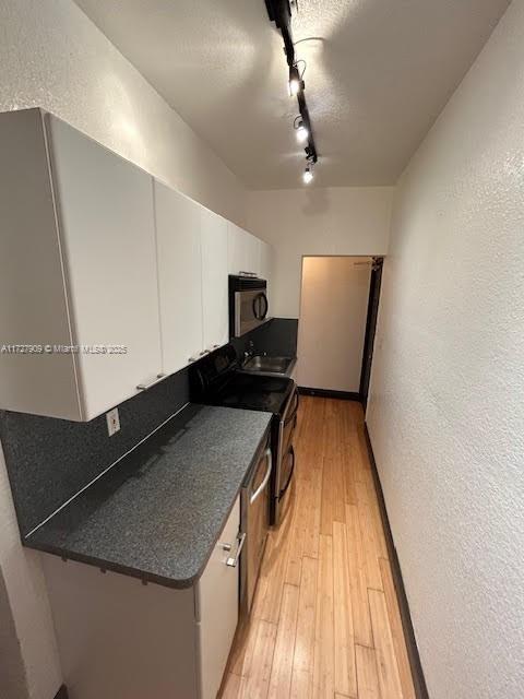 kitchen with rail lighting, sink, light wood-type flooring, white cabinets, and range