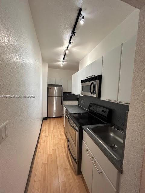 kitchen featuring appliances with stainless steel finishes, track lighting, white cabinets, light hardwood / wood-style flooring, and sink