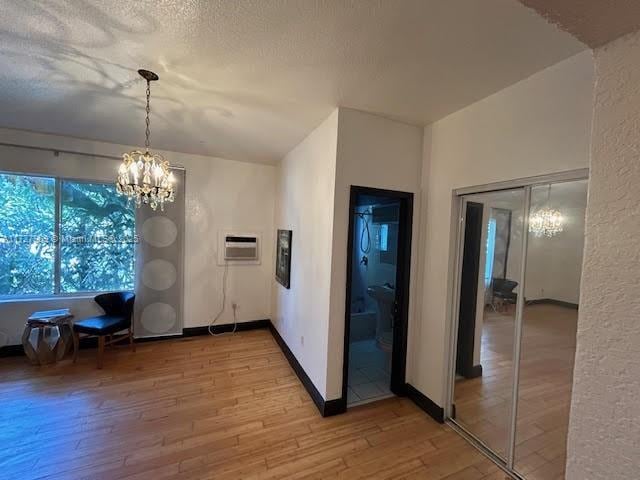 unfurnished dining area with a wall mounted air conditioner, a notable chandelier, a textured ceiling, and hardwood / wood-style floors