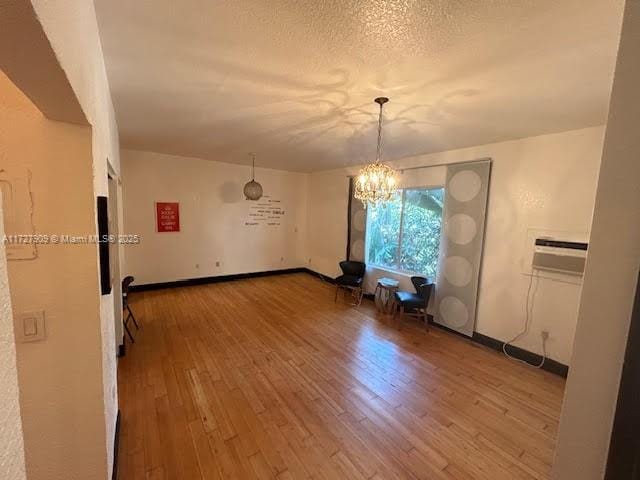 unfurnished dining area with a textured ceiling, a chandelier, hardwood / wood-style flooring, and a wall mounted air conditioner