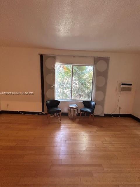 unfurnished room with a textured ceiling, light hardwood / wood-style flooring, and a wall mounted air conditioner