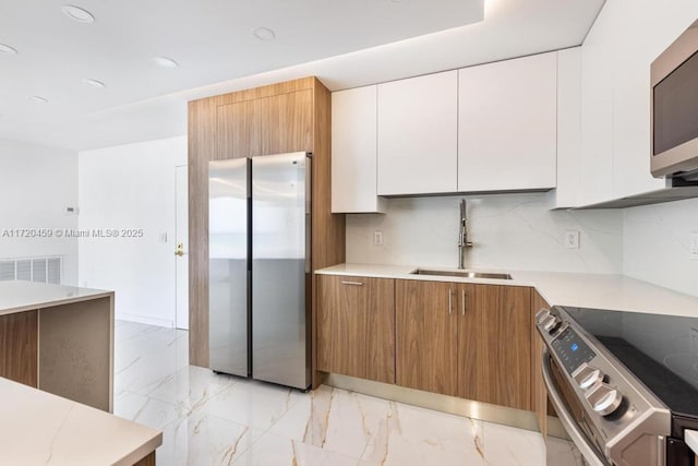 kitchen featuring white cabinets, backsplash, appliances with stainless steel finishes, and sink