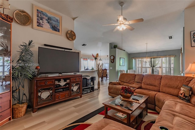 living room featuring lofted ceiling, light wood-type flooring, and ceiling fan with notable chandelier