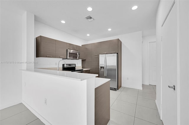 kitchen with light tile patterned floors, dark brown cabinetry, appliances with stainless steel finishes, and kitchen peninsula