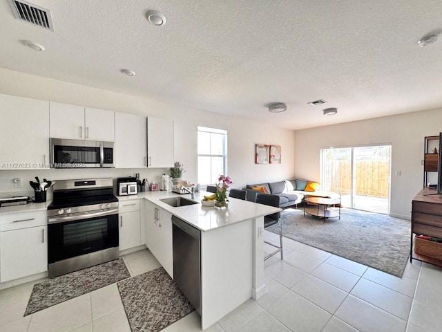 kitchen with white cabinets, stainless steel appliances, sink, kitchen peninsula, and light tile patterned floors