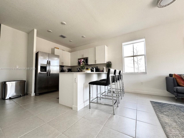 kitchen with kitchen peninsula, appliances with stainless steel finishes, white cabinetry, light tile patterned floors, and a kitchen bar