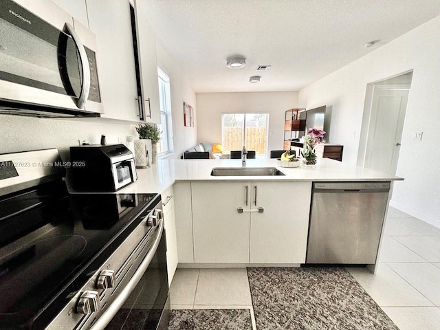 kitchen featuring kitchen peninsula, appliances with stainless steel finishes, sink, light tile patterned floors, and a textured ceiling