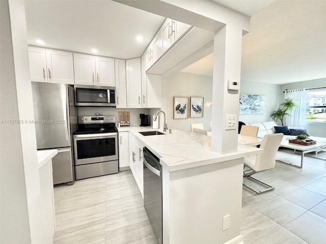 kitchen with sink, white cabinetry, stainless steel appliances, light stone countertops, and kitchen peninsula