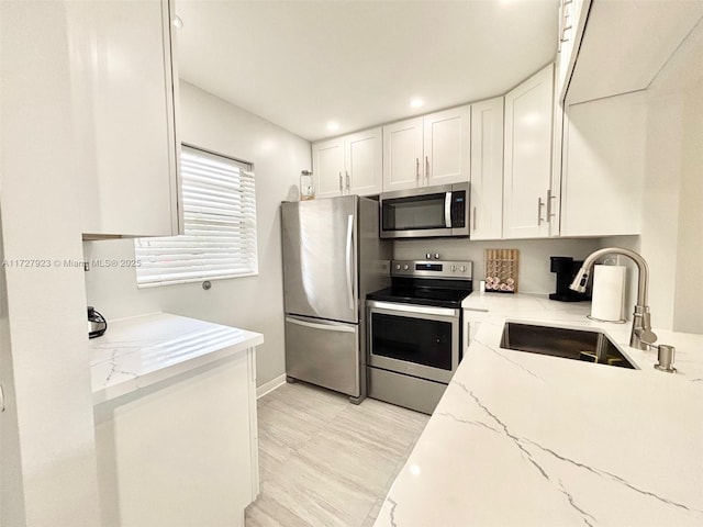 kitchen featuring stainless steel appliances, white cabinetry, sink, and light stone counters