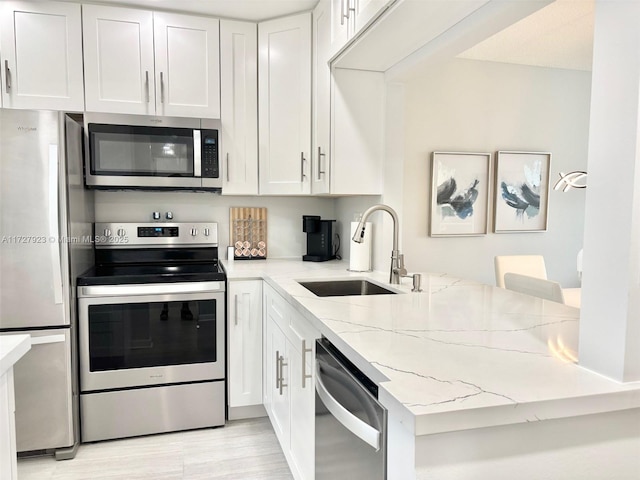 kitchen with sink, a breakfast bar, white cabinetry, stainless steel appliances, and light stone countertops