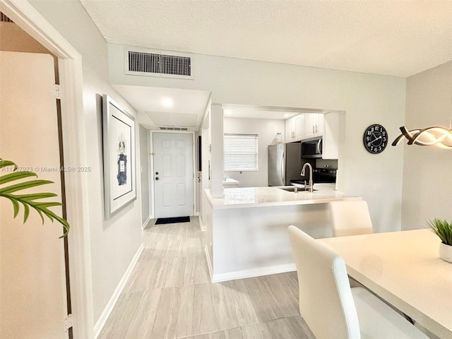 kitchen with sink, appliances with stainless steel finishes, white cabinetry, a textured ceiling, and kitchen peninsula