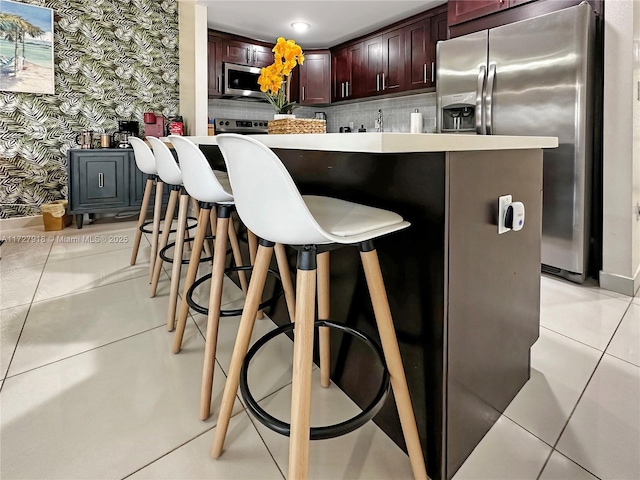 kitchen with light tile patterned floors, appliances with stainless steel finishes, a kitchen bar, and sink