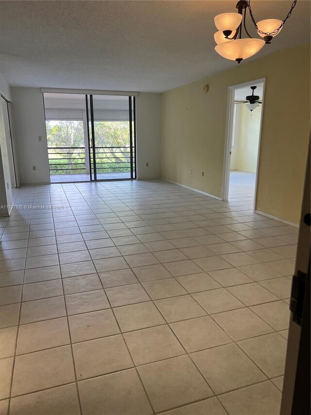 tiled spare room featuring ceiling fan with notable chandelier