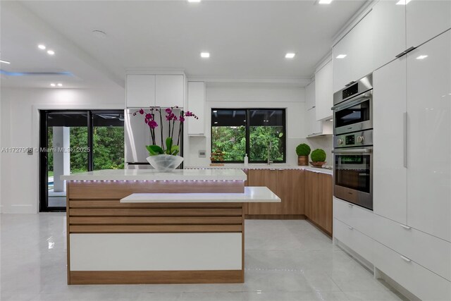 kitchen with a healthy amount of sunlight, appliances with stainless steel finishes, a center island, and white cabinets