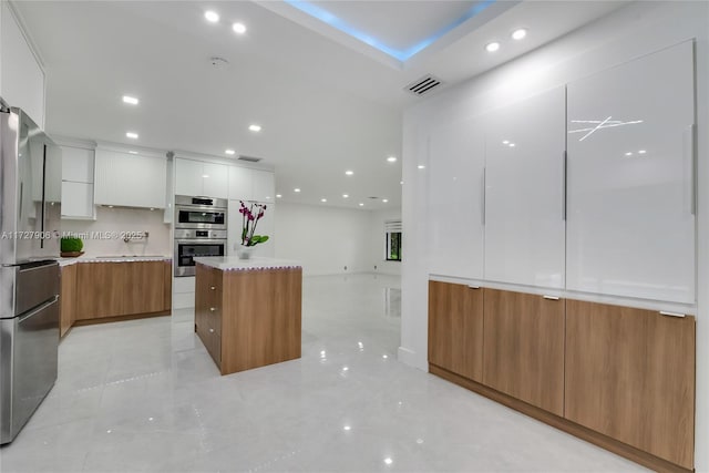 kitchen with stainless steel appliances, a large island, white cabinets, and decorative backsplash