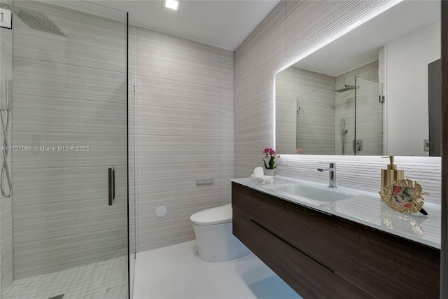 bathroom with a shower with door, vanity, tile walls, and toilet