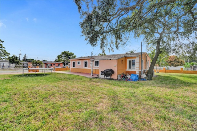 back of property with a trampoline, a yard, and a patio