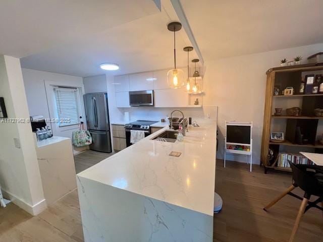 kitchen featuring light hardwood / wood-style floors, appliances with stainless steel finishes, white cabinetry, hanging light fixtures, and sink