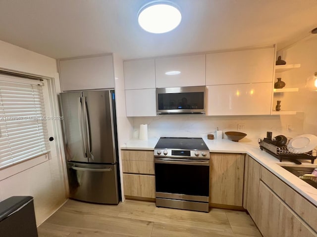 kitchen featuring light wood-type flooring, stainless steel appliances, white cabinets, and light brown cabinets