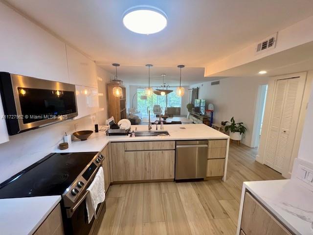 kitchen featuring pendant lighting, stainless steel appliances, light brown cabinetry, light hardwood / wood-style floors, and kitchen peninsula