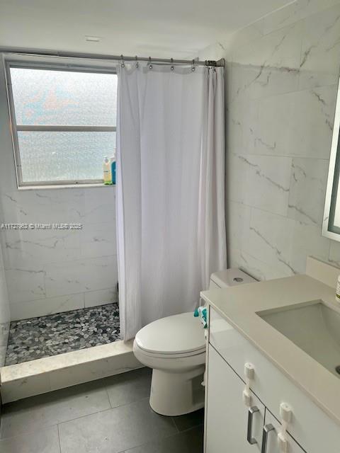 bathroom with tile patterned floors, tile walls, a shower with curtain, toilet, and vanity