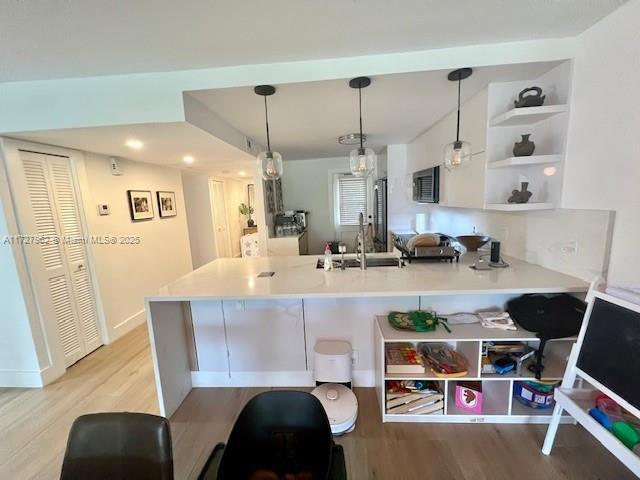 kitchen with kitchen peninsula, hanging light fixtures, sink, built in features, and light wood-type flooring