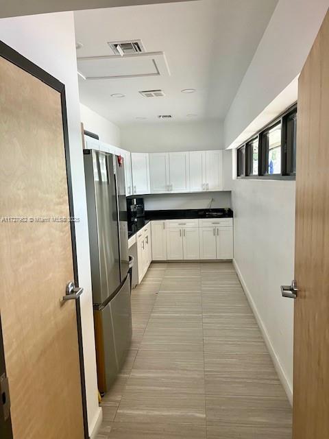 kitchen with light tile patterned flooring, white cabinets, and stainless steel refrigerator