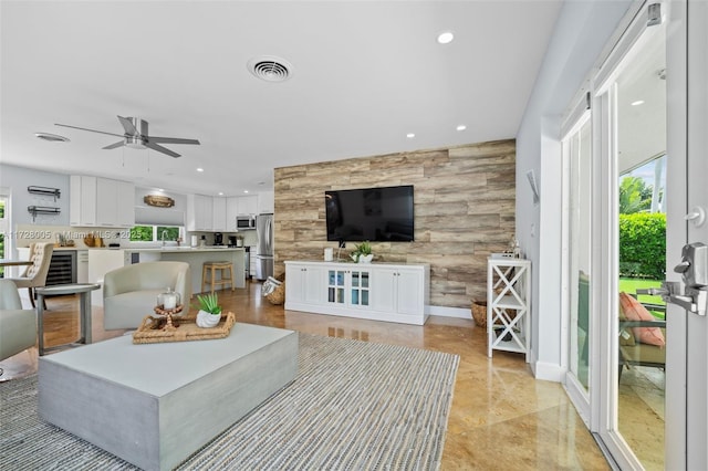 living room with ceiling fan, wine cooler, wood walls, and sink